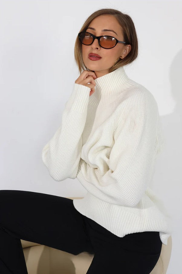 Woman wearing a white turtleneck sweater and black pants against a white background