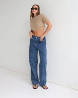 Woman wearing a beige fluffy knit crop top and blue jeans against a white background