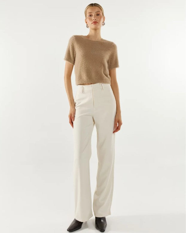 Woman wearing a beige fluffy knit top and white pants on a white background