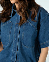 Close-up of a person wearing a blue denim short-sleeve button-up shirt with two chest pockets and contrast stitching.