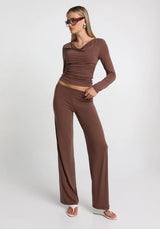 Woman wearing a brown long sleeve top and straight leg brown pants on a white background