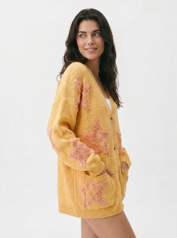 Woman wearing a yellow cardigan with pink star patterns on a white background