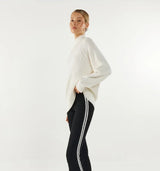 Woman wearing a white turtleneck sweater and black leggings with white stripes on a light grey background