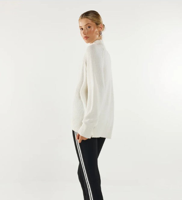 Woman wearing a white turtleneck sweater and black pants with white stripes on a light grey background