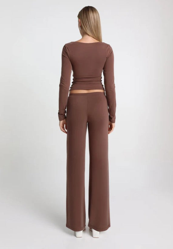 Person wearing a brown long sleeve top and straight leg brown pants on a white background