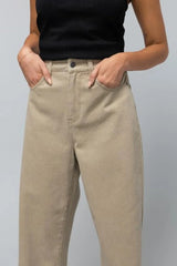 close up of beige coloured denim jeans with the model with her hands in the front pockets on a white background