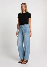 model with blonde hair wearing a black short sleeve top and light denim barrel jeans on a white background
