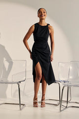Woman in a black dress standing between two clear chairs against a white background