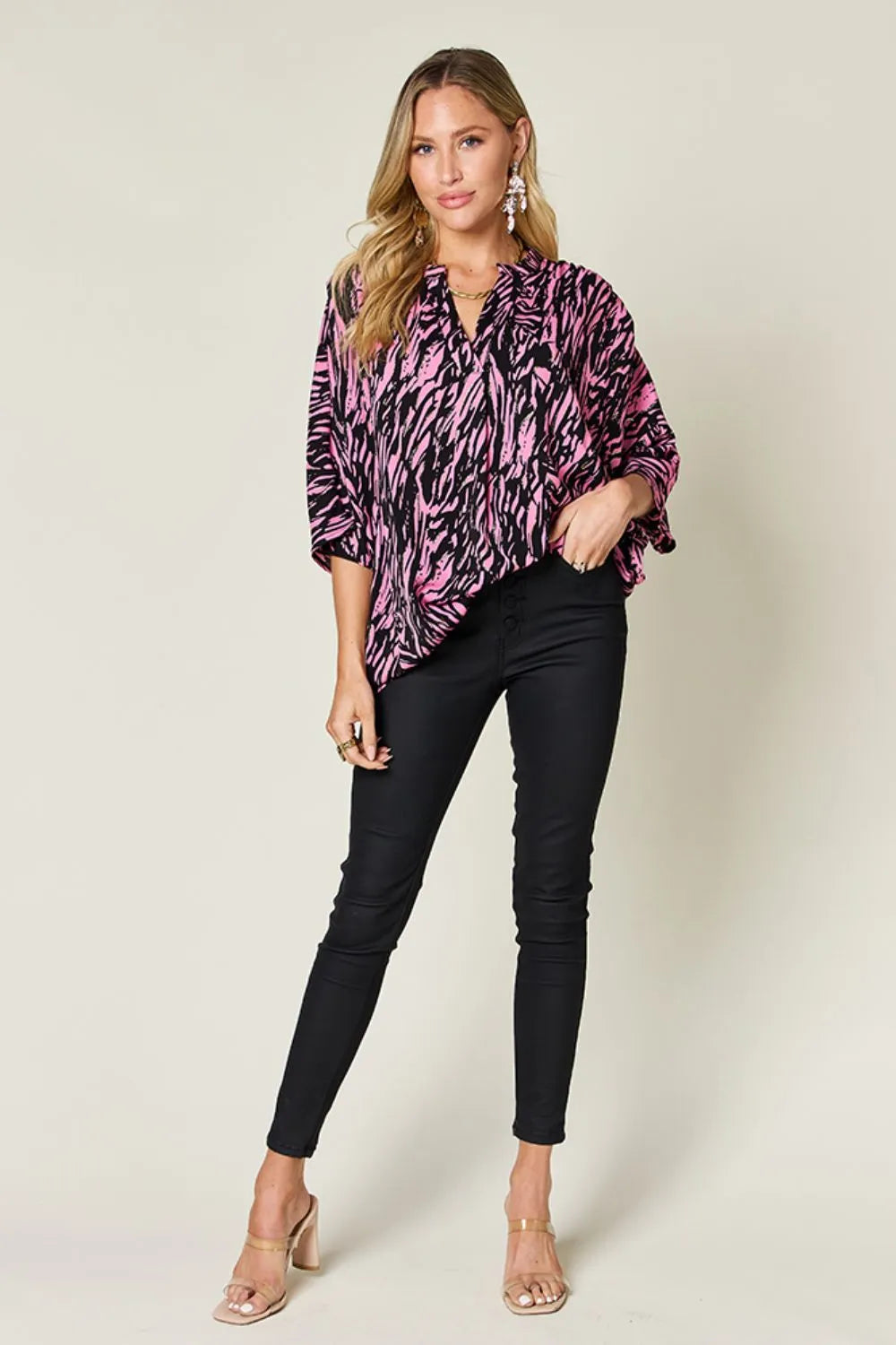 Woman wearing a pink and black patterned blouse with black pants on a white background