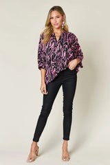 Woman wearing a pink and black patterned blouse with black pants on a white background