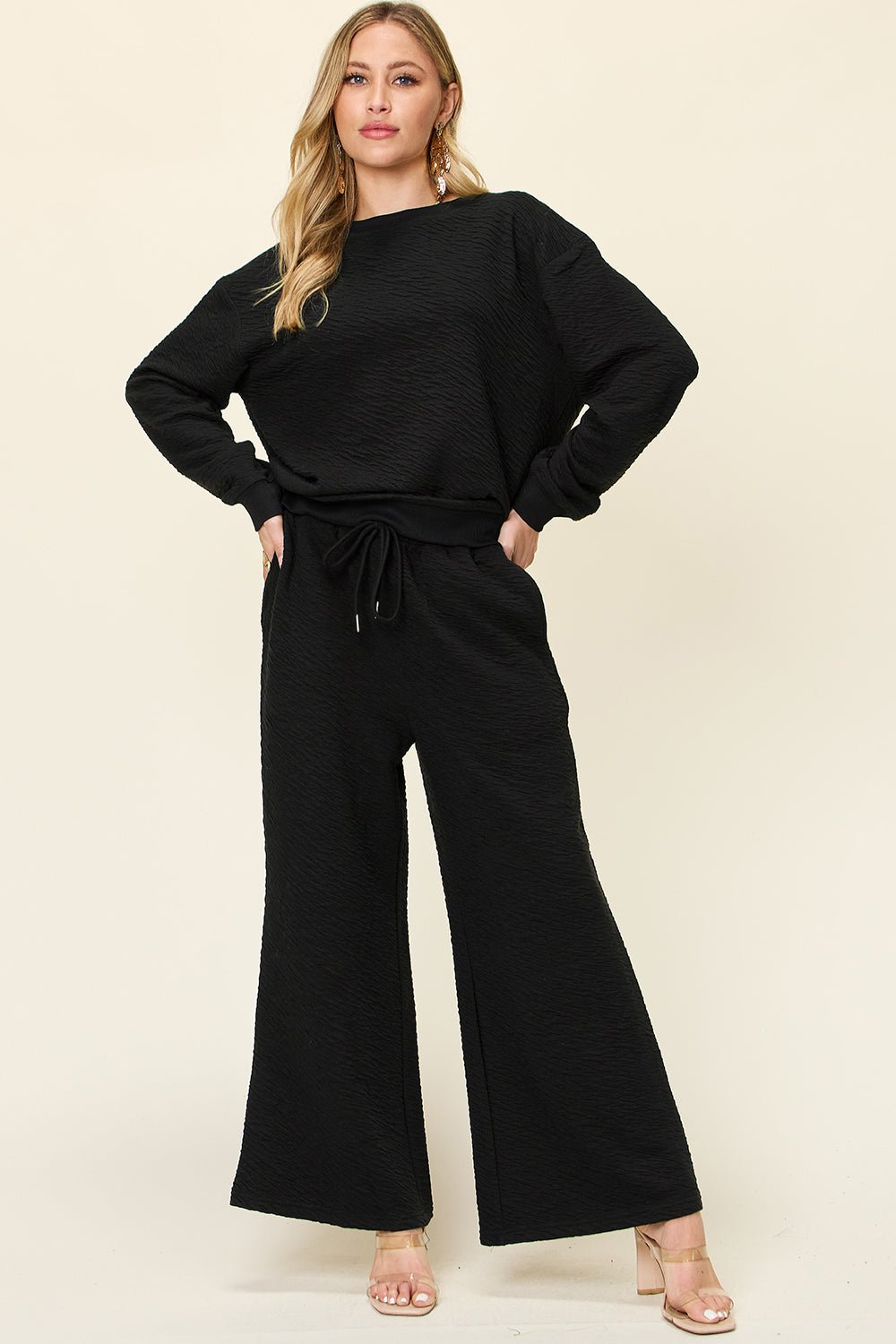 Woman wearing a black outfit with wide-leg pants on a beige background