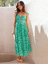 Woman wearing a green patterned dress standing against a textured wall.