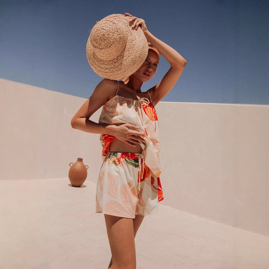 A model wearing the Cali Shorts and Top Two Piece Set in a tropical print, styled with a wide-brim straw hat.