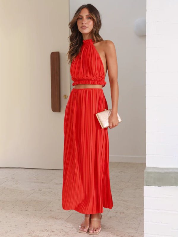 A model wearing the Calista Skirt and Top Two Piece Set in red, featuring a pleated maxi skirt and halter neck top.
