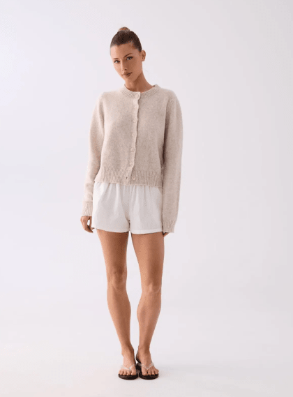 Woman wearing a beige cardigan and white shorts on a white background