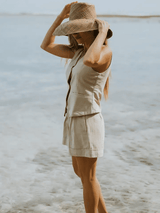 Model adjusting her hat while wearing the Cate Shorts set at the shoreline, showing relaxed summer styling.