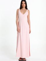 A woman modelling a light pink sleeveless maxi dress with a V-neckline and a high side slit, paired with black sandals, against a plain white studio background.