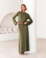 Full-length view of the olive green Cora Knit Set styled with a tie-waist skirt and off-shoulder knit top.