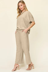 Woman wearing a beige loungewear pants and top set with a plain background