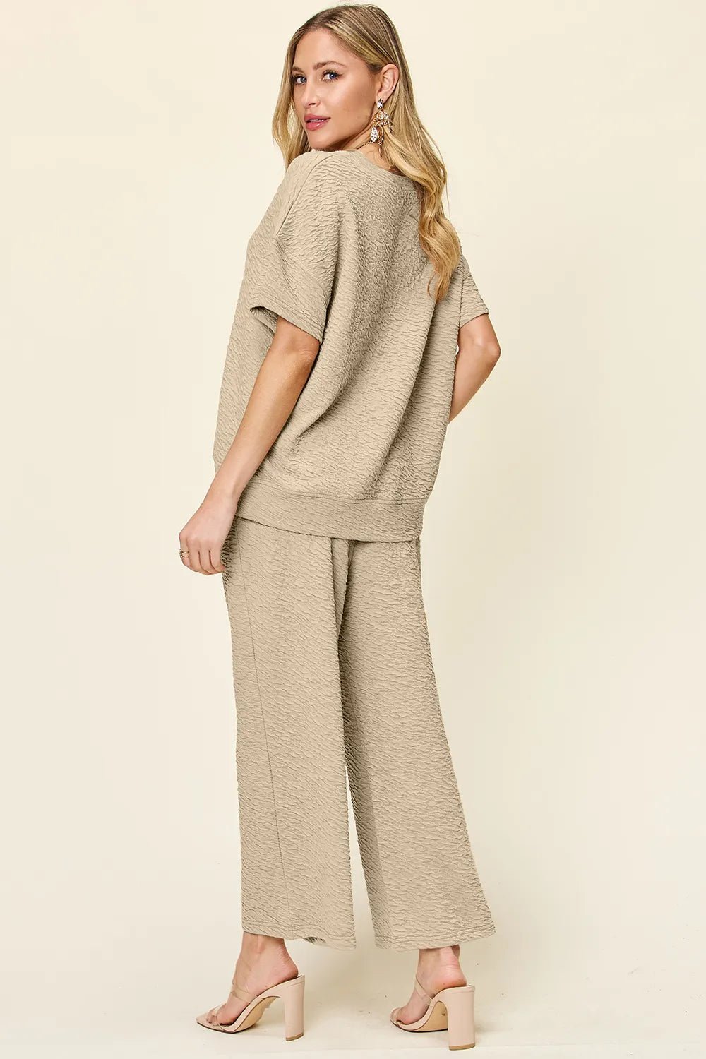 Woman wearing a beige loungewear pants and top set with wide-leg pants on a plain background