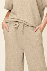 Woman wearing a beige textured loungewear set with a top and pants on a neutral background