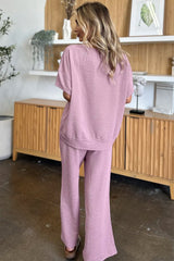 Woman wearing a pink loungewear pants and top set standing in a room with wooden furniture and decor.
