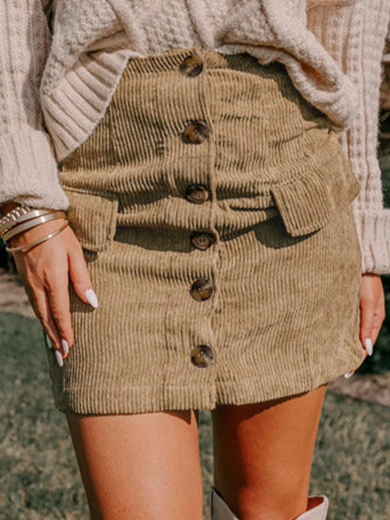 Woman wearing tan corduroy mini skirt with knit sweater and hands in pockets