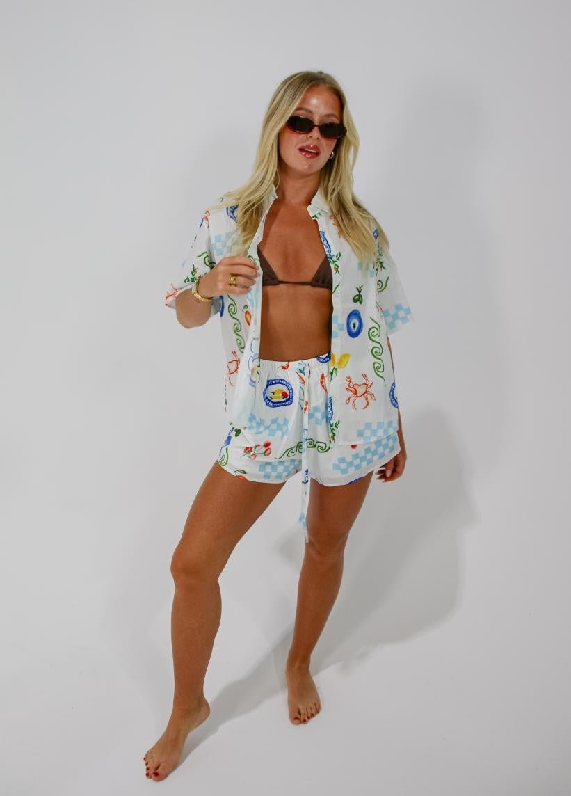 Standing pose of woman wearing Greco Shorts and Top Set with open shirt over a bikini top.