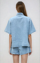 Model wearing the light blue version of the denim two piece set, facing backwards with hair tied back.