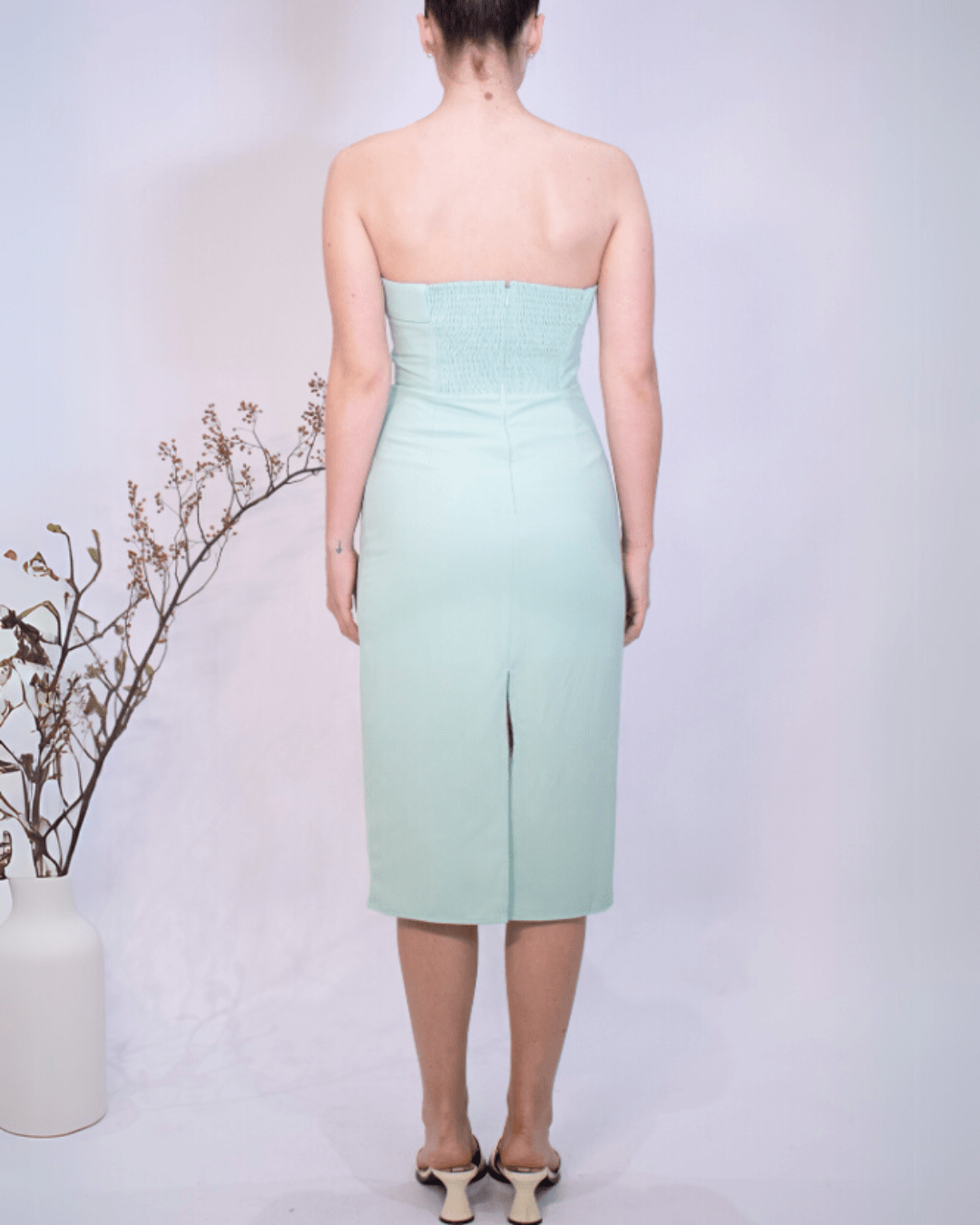 Woman wearing a strapless light green dress with a slit on a plain background