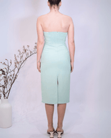 Woman wearing a strapless light green dress with a slit on a plain background