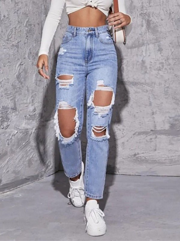 Person wearing ripped blue jeans and white sneakers against a gray background
