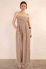 Woman wearing a beige striped spaghetti strap jumpsuit against a plain background