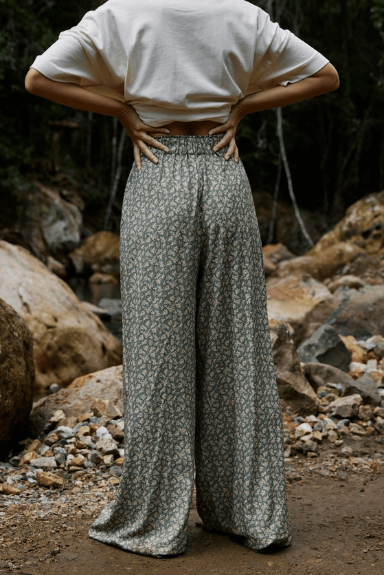 Person wearing a white shirt and patterned pants standing in a natural setting with rocks and foliage.