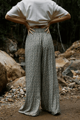 Person wearing a white shirt and patterned pants standing in a natural setting with rocks and foliage.