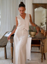 Woman in a beige sleeveless top and beige maxi skirt standing in a dining room.