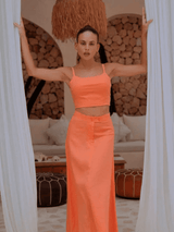 Model wearing the Marie Maxi Skirt and matching Jessica Top in peach, standing in a linen-draped doorway.