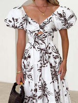 Woman wearing a white dress with black floral pattern against a plain background