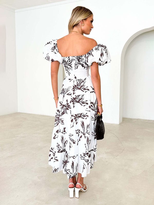 Woman wearing a white off-shoulder dress with black floral pattern in a minimalistic room.