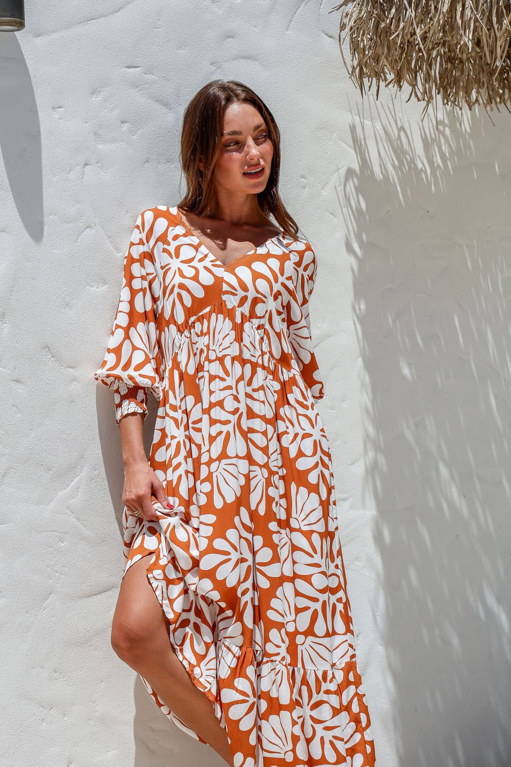 Woman wearing an orange and white floral dress against a white wall.