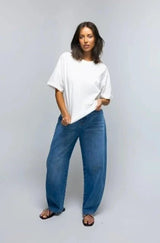 Woman wearing a white t-shirt and blue jeans against a plain background