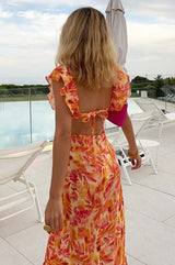 Woman in a colorful dress standing on a rooftop with a view of a pool and greenery.