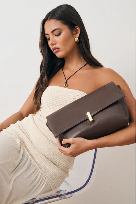 Woman holding a brown clutch bag against a plain background