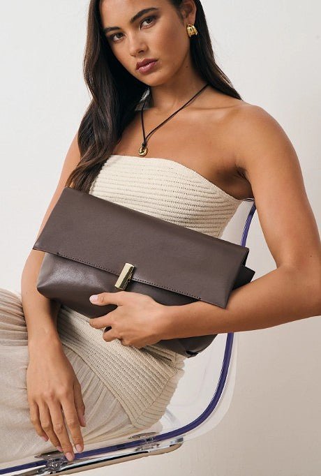 Woman holding a brown clutch bag against a neutral background