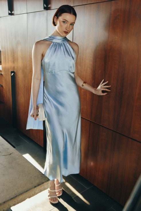 Woman in a light blue dress standing against a wooden wall.