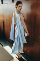 Woman in a light blue dress standing against a wooden wall.