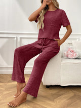 Woman wearing a maroon  textured pants and top set sitting on a white couch.