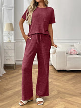 Woman wearing a burgundy  textured pants and top set in a living room setting