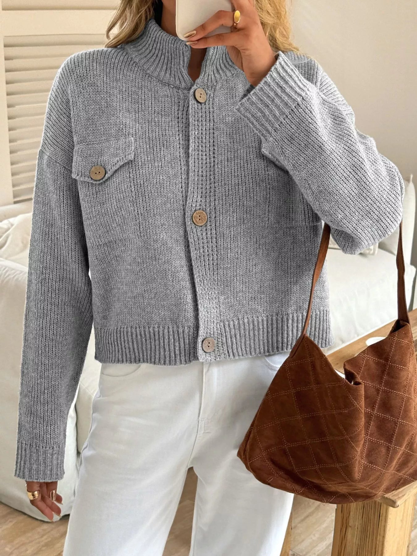 Person wearing a light blue knitted cardigan with a brown bag in a neutral setting