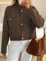Person wearing a brown knitted cardigan holding a brown handbag indoors.